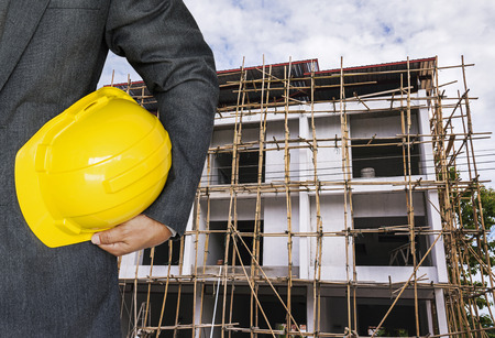 Engineer hand holding yellow helmet for workers security against the background of building under construction の写真素材