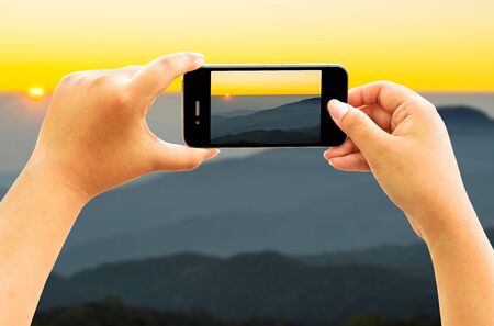 Smart phone taking photo of Mountain ranges and sunrise ,Doi Inthanon National Park, Chiang Mai,Thailand.の写真素材