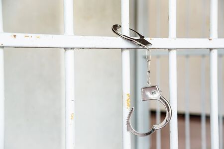 Closeup of unlocked handcuffs hanging on jail barsの写真素材