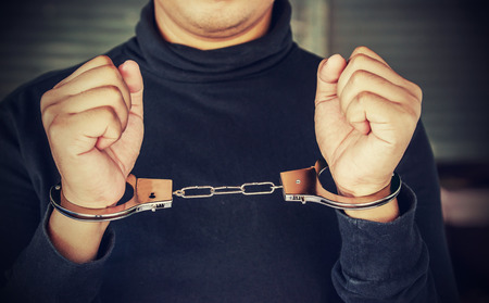 Man holding his head and hands locked in handcuffs. Vintage Filter Effect.