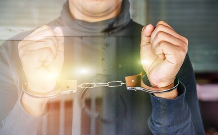 Double exposure of male hands locked in handcuffs with jail bars background, Outlaw's hands in handcuffs.の写真素材