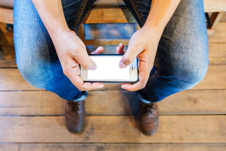 Male with a phone in his hands sitting on the wooden chair from top view, Man's hands holding smart...