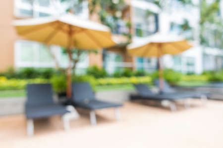 Abstract blur outdoor swimming pool, umbrella and wood bench.