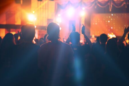 Young people dancing and cheering in front of bright stage lights, Silhouettes of concert crowd.