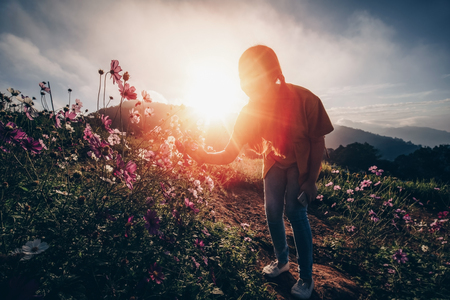 Sillhouette of a young girl enjoying in the cosmos flower garden against sunset or sunrise, selective focus and vintage filterの写真素材