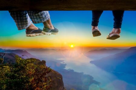 Mother and daughter sit on a wooden bridge and hang their legs to watch the sunrise in the morning.の写真素材