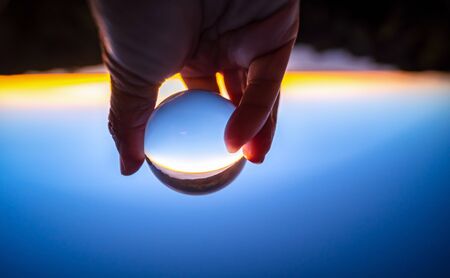 Closeup of the hand holding a glass ball reflecting the sunrise and mountain. Concept of...