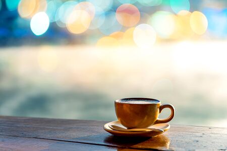 Hot coffee cup on wooden table with warm sunlight and the misty at lake in morning against blurred Chinese village in Mae Hong Son, Thailandの写真素材