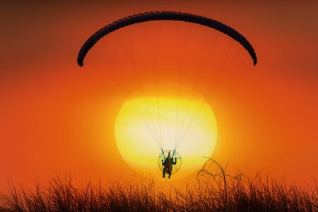 Silhouette of para motor glider flying in the orange sky,  Selective Focus.の写真素材
