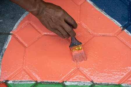 Close-up Hand woman painting a floor with orange oil paint at homeの写真素材