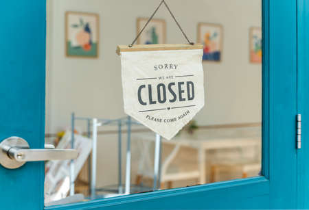 Close sign and chain hangs on a glass storefront or door due to the shop or retail business being...
