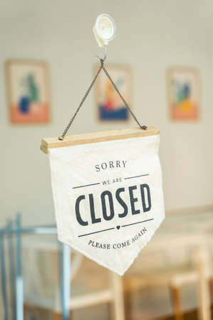 Close sign and chain hangs on a glass storefront or door due to the shop or retail business being...