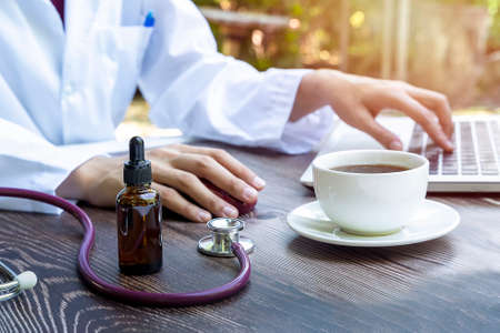 Close up of dropper with CBD oil on desk, Work of the scientist with Marijuana tea , Laptop, Stethoscope - Medical marijuana conceptの写真素材
