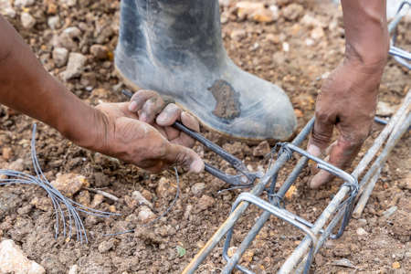 Hands of the workers are binding the wire with steel bars at the construction site, knitting metal rods with steel bars for concreteの写真素材
