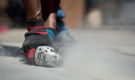 Worker in gloves with a small angle grinder cuts fibre cement, concrete plate in construction site. Builder worker cutting granite slab with using a cut-off sawの写真素材