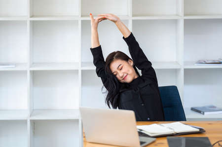 Work from home, Stretch for relax, Young Asian business woman raise arm up and close eye while working with laptop computer at her desk home office, Portrait of beauty happy woman stretching body while working with laptopの写真素材