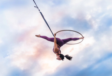 Asian beautiful woman doing aerial hoop or aerial ring practice outdoor. Woman hanging in aerial ring in the bright skyの写真素材