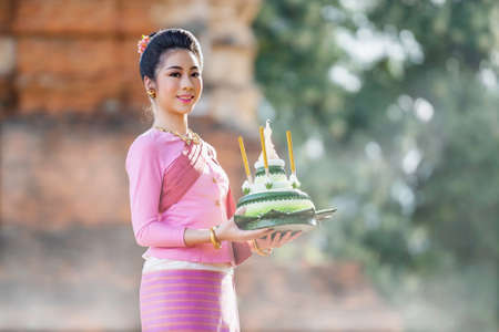 Beautiful woman dressed in Thai national costumes and put the krathong on the hand, Loy krathong tradition that paid respects to the water spirits. The word krathong refers to basket and loy means to floatの写真素材