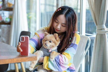 Friendship and happiness Concept. Young beautiful woman taking selfie with her dog at home. Pomeranian Spitz selfie with ownerの写真素材