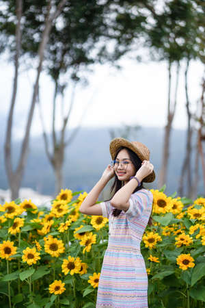 young asian woman wearing a straw hat and smiling happily in the sunflower fieldの写真素材