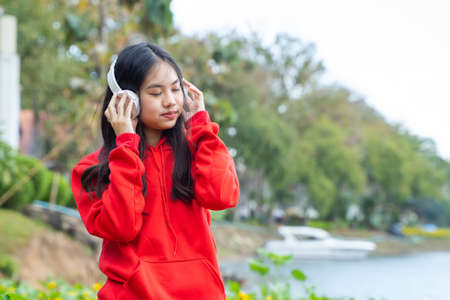 beautiful woman wearing a red long-sleeved shirt with close eyes and listens to music, enjoys a blooming sunflower field in summer.の写真素材