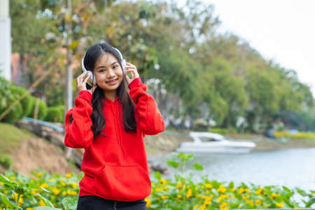 beautiful woman wearing a red long-sleeved shirt listens to music and enjoys a blooming sunflower fieldの写真素材