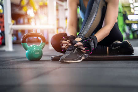 Young girl asian knelt down to do up her shoelaces at fitness gym after training sport with dumbbellの写真素材