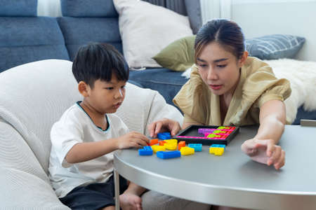 Young Asian mother playing with colourful blocks toy with her son at home. Mom and her son are playing with different developing toysの写真素材