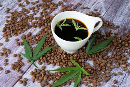 Cannabis coffee - marijuana leaf on coffee cup and coffee beans. Coffee with herbal ingredients, cannabis drink concept.の写真素材