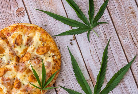 Homemade pizza with marijuana or cannabis leaves on wooden background. Fresh medical marijuana, cannabis decorate on pizza.の写真素材