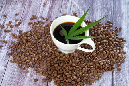 Cannabis coffee - marijuana leaf on coffee cup and coffee beans. Coffee with herbal ingredients, cannabis drink concept.の写真素材