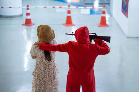 Terrorist wearing red costume holding gun kidnapping young women for a hostage in abandoned building. Concept of rape, terrorism, crime, violence, robbery and killの写真素材