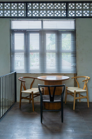 The wooden table and chairs near the window in cafe with sunlight through the window blind sunshade. Empty chairs and table with light and shadow in the room.の写真素材
