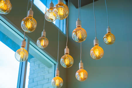 Vintage tungsten filament multiple lamps hanging from the ceiling on a white wires as an interior...