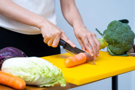 Young woman cutting vegetables in the kitchen. Woman's hands cutting vegetables, behind fresh vegetables. asian woman uses a knife and cooks.の写真素材