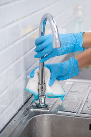 Close up of female hand in protective gloves blue wiping dust using spray and cloth while cleaning her kitchen.Cleaning and housekeeping conceptの写真素材