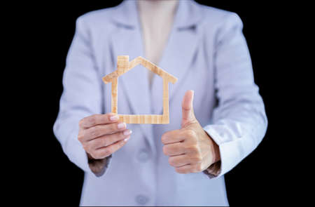 Hand holding a wooden miniature home, woman hand symbolically holds a mini wood house. Wooden house in female hands in black. Construction conceptsの写真素材