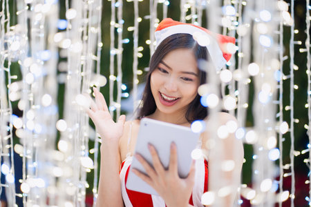 Christmas time concept. Young woman in Santa Claus dresse and  hat with tablet pc laptop near the Christmas tree. doing online shopping, buying browsing for gifts, having funの写真素材