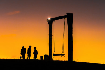 silhouette of happy young man and woman on hadubi hill and a swing with golden light sunset background. Hadubi viewpoint at Lao Wu village ,Wiang Haeng, Chiang Mai, Thailand.Copy space for inscriptionの写真素材