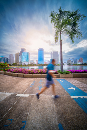 BANGKOK, THAILAND - December 04, 2022 : Man jogging in park at Benjakitti Park , Benchakitti Forest Park and the skyscraper business district the morning at Bangkok, Thailand. Healthy lifestyle conceptのeditorial素材
