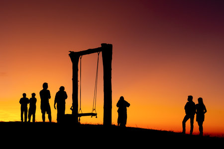 Group of people on top of a mountain in sunset. Silhouette of friends on hill and swing with golden sunset background. hikers celebrating success on top of a hill in the sunsetの写真素材