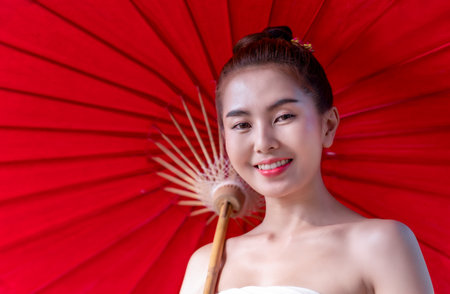 Beautiful Asian girl wearing traditional northern dress costume holding red umbrella as countryside, Thai Woman in Traditional Costume of Chiang Mai, Thailand. Identity culture of Thailandの写真素材