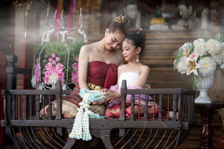 Portrait of beautiful woman in Thai old suit or Thai national dress looks elegant and charming and a little girl sit on ancient elephant seat in old antique Thai houses, Old Thai fashion model conceptの写真素材