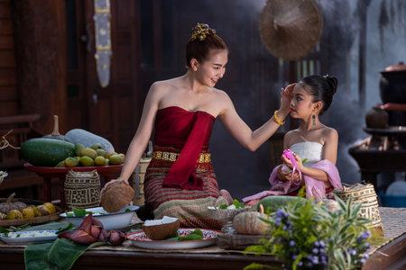 Beautiful woman teaching little girl to cooking Thai culture style. Asian woman wearing Thai dress costume traditional according culture and tradition cooking in kitchen at the ancient house Thailandの写真素材