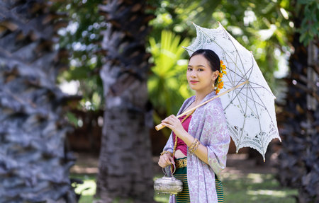 Beautiful Asian women wearing in Thai dress Lanna style costume traditional according walk with a garland flower and umbrella in Wat Ton Kwen Temple Chiang Mai, Thailand. the ancient wooden templeの写真素材
