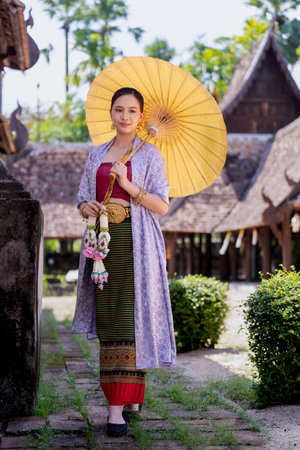 Beautiful Asian women wearing in Thai dress Lanna style costume traditional according walk with a garland flower and umbrella in Wat Ton Kwen Temple Chiang Mai, Thailand. the ancient wooden temple dress and Thai houseの写真素材