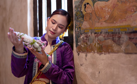 Asian beautiful lady wearing in Thai dress costume traditional according Thai culture and tradition holding Thai Jasmine garland at the ancient wooden temple Chiang Mai, Thailand. Portrait Thai womanの写真素材