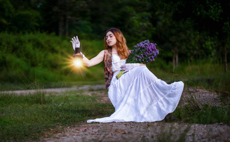 A beautiful woman in a white dress holding a lantern in a forest outside before night. scary scene
