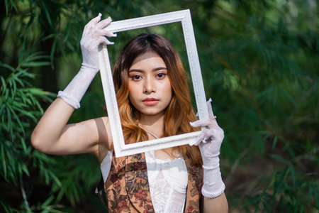 Young Asia woman with white dress holding an empty frame in front of her face in nature the...