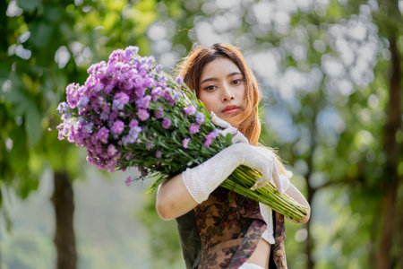 a young woman in a white dress stands on a green field and holds a large bouquet of flowers in her hands. In the background, there are forest and a lake. Lifestyle concept.の写真素材